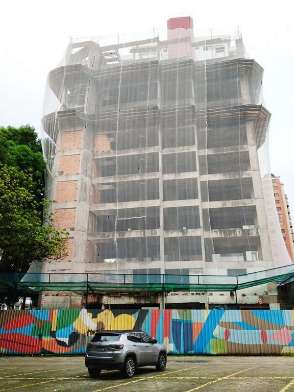 Edifício de vários pavimentos envolto em tela de proteção durante demolição controlada