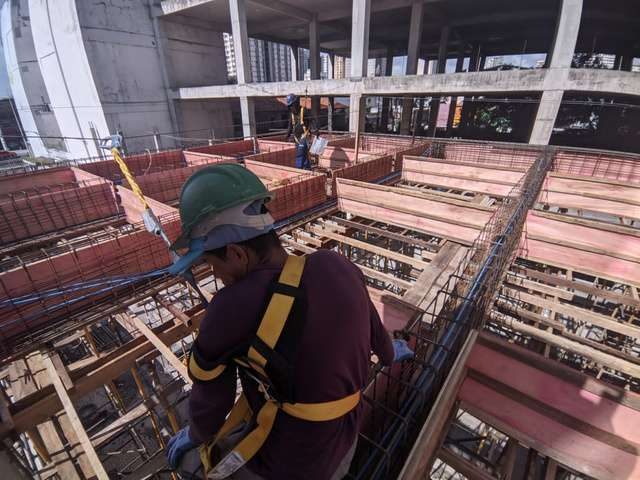 Operário com cinto de segurança montando armadura de laje protendida